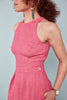 A woman wearing a pink jumpsuit with princess seams on the bodice, a fitted waistband and culotte style shorts. The jumpsuit is bathroom-friendly and has pockets